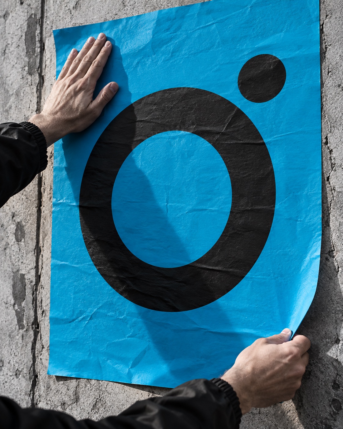 Imagen editorial: manos colocando un cartel azul con una composición gráfica circular